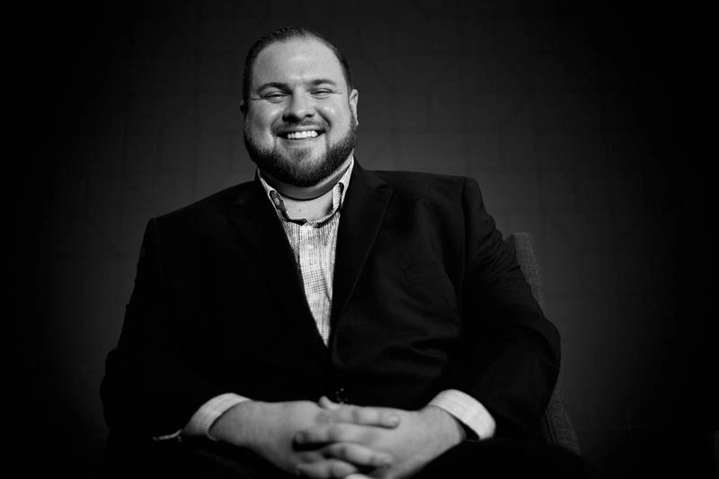 Black and white photo of a bearded man in a suit smiling broadly with hands clasped