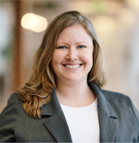 A woman in a grey jacket and white shirt smiles for the camera