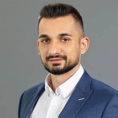 A man with a beard is wearing a blue suit and white shirt