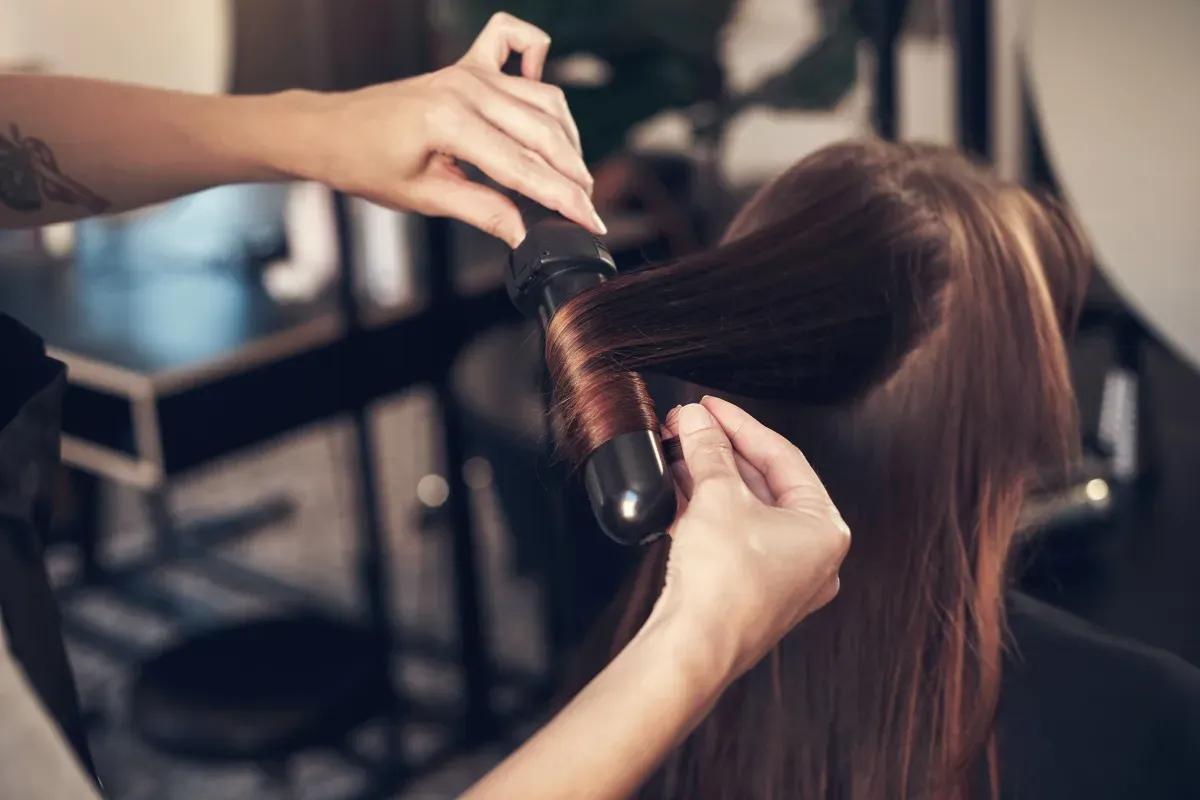 A woman is getting her hair straightened by a hairdresser in a salon
