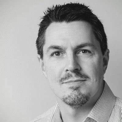 A black and white photo of a man with a beard wearing a striped shirt