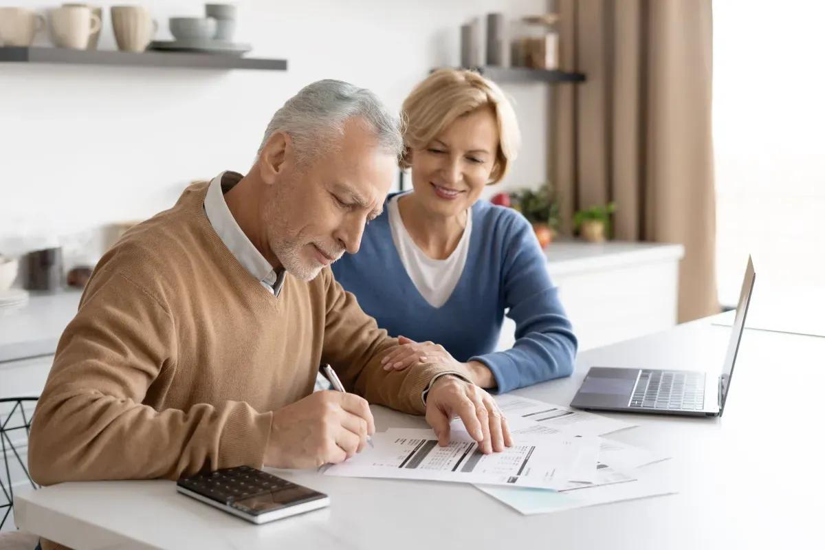 An elderly couple is sitting at a table with a laptop and a calculator