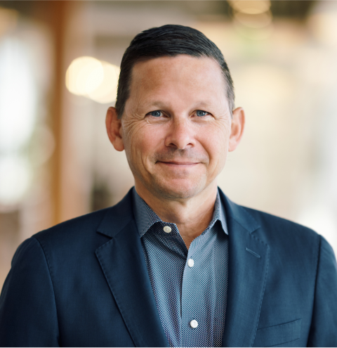 A man wearing a blue jacket and a polka dot shirt smiles for the camera