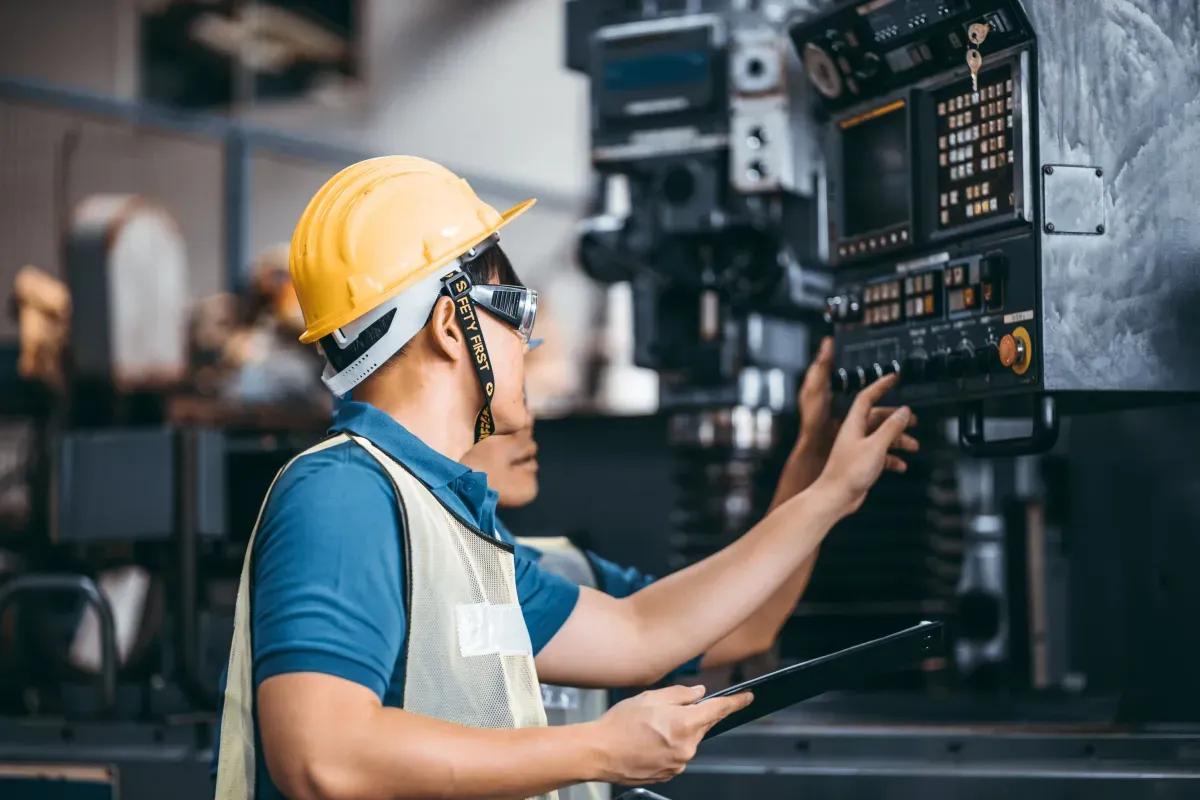 A man wearing a hard hat and safety vest is working on a machine in a factory