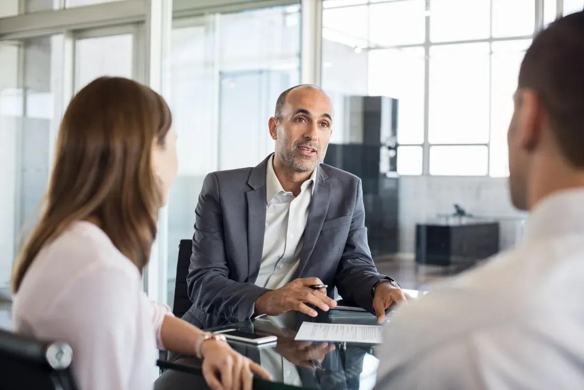 A man in a suit is sitting at a table talking to two people