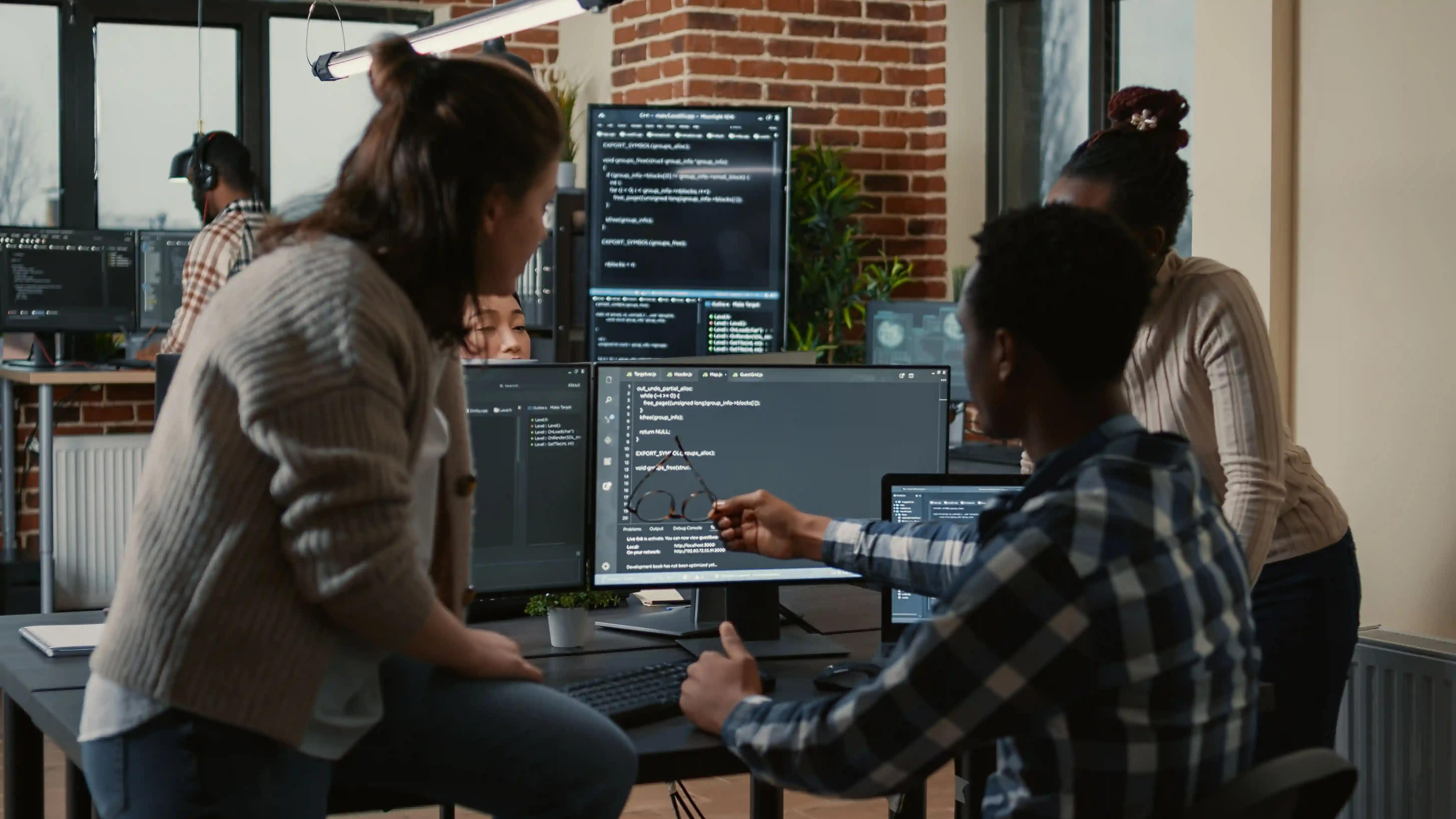 A group of people are sitting at a desk using laptops and computers