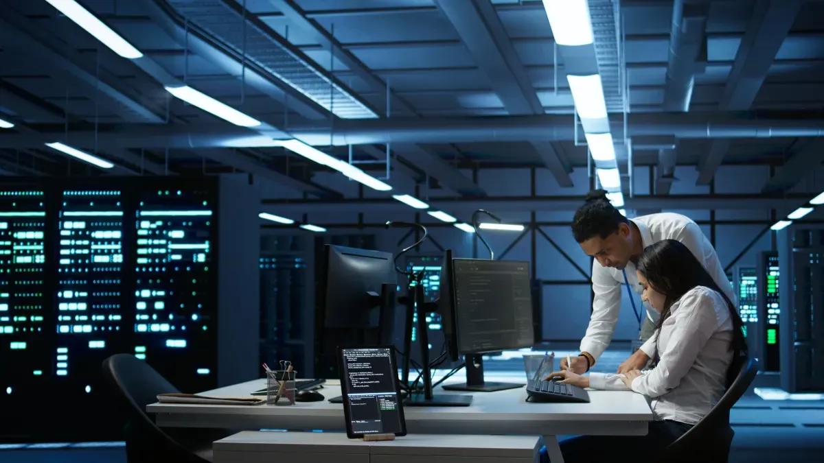 A man and a woman are working on a computer in a server room