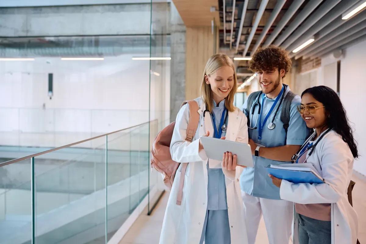 A group of doctors are standing in a hallway looking at a tablet