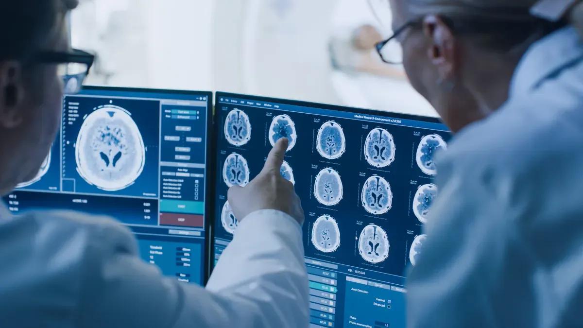 Two doctors are looking at a ct scan of a brain on a computer screen