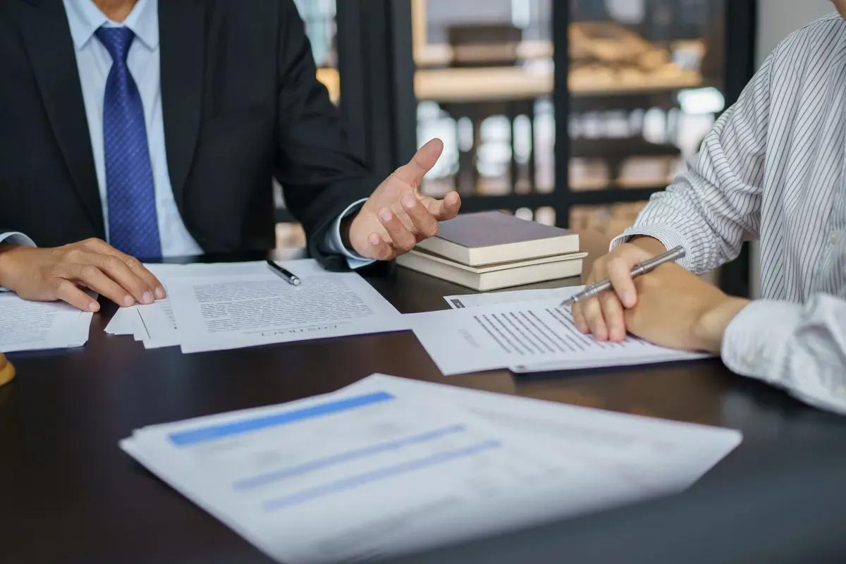 A man in a suit and tie is sitting at a table with a woman signing a document