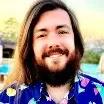 A man with a beard and long hair is wearing a blue shirt and smiling