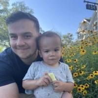 A man is holding a baby in his arms in front of a field of flowers