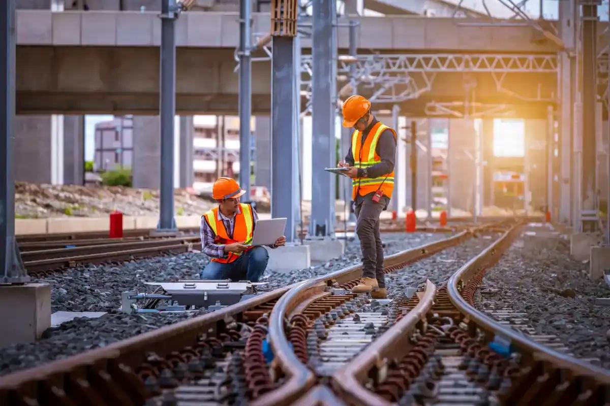 Two construction workers are working on train tracks