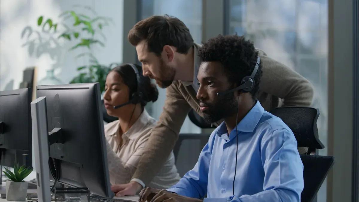 A man and a woman wearing headsets are looking at a computer screen