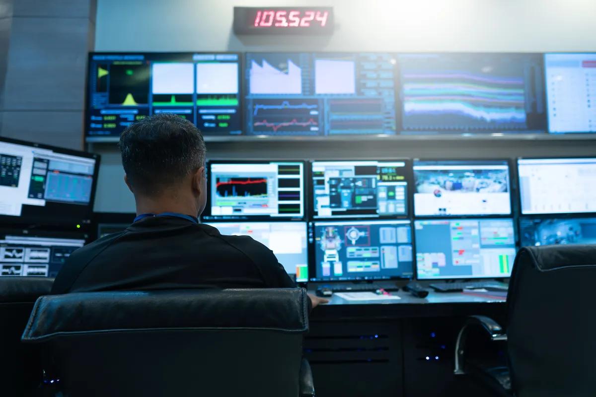 A man is sitting in front of a bunch of computer monitors in a control room
