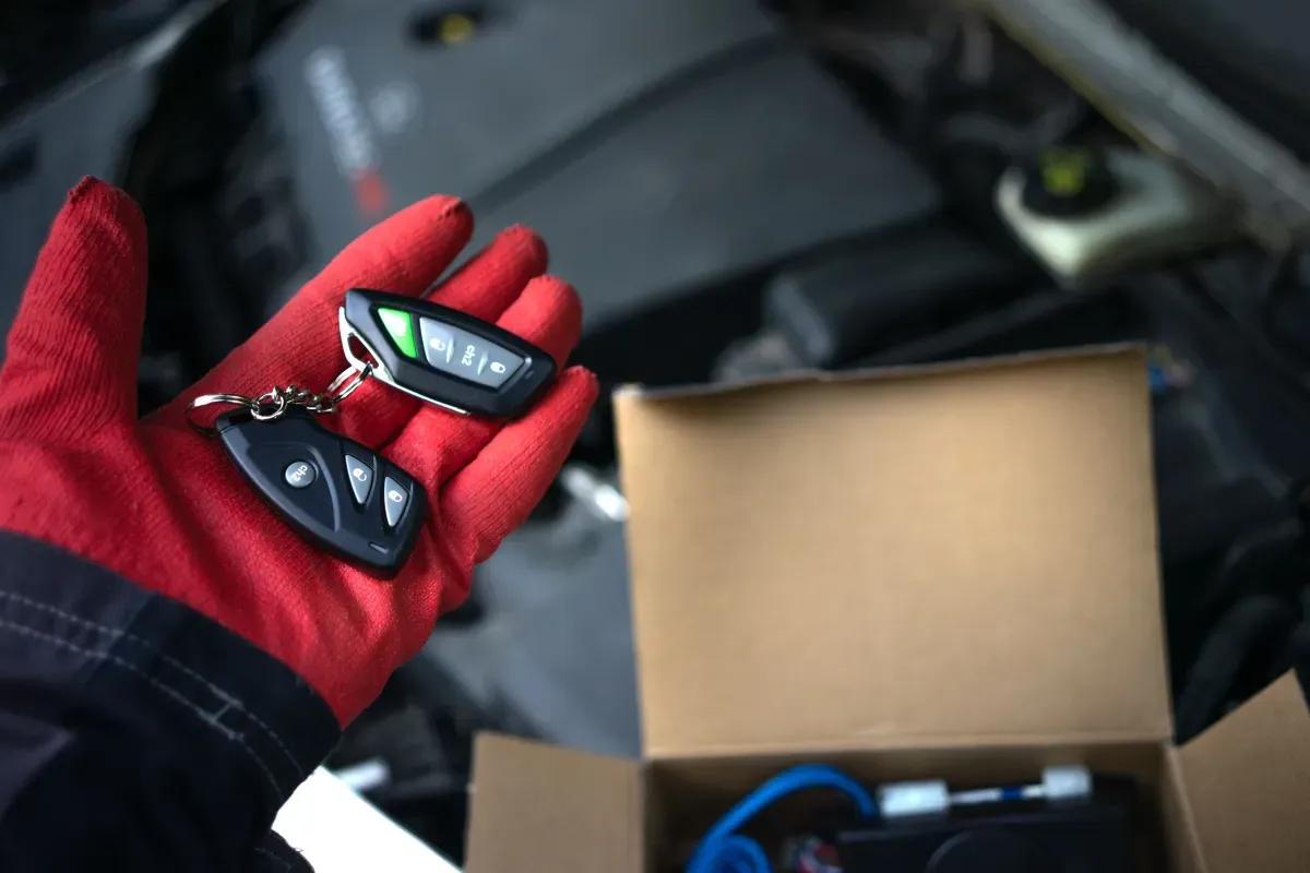 A person is holding a remote control in their hand in front of a car engine