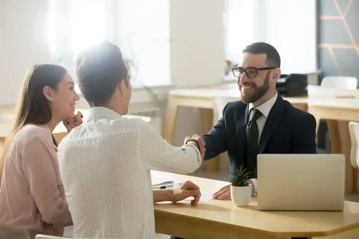 Un homme et une femme se serrent la main avec un homme en costume tout en tant assis une table
