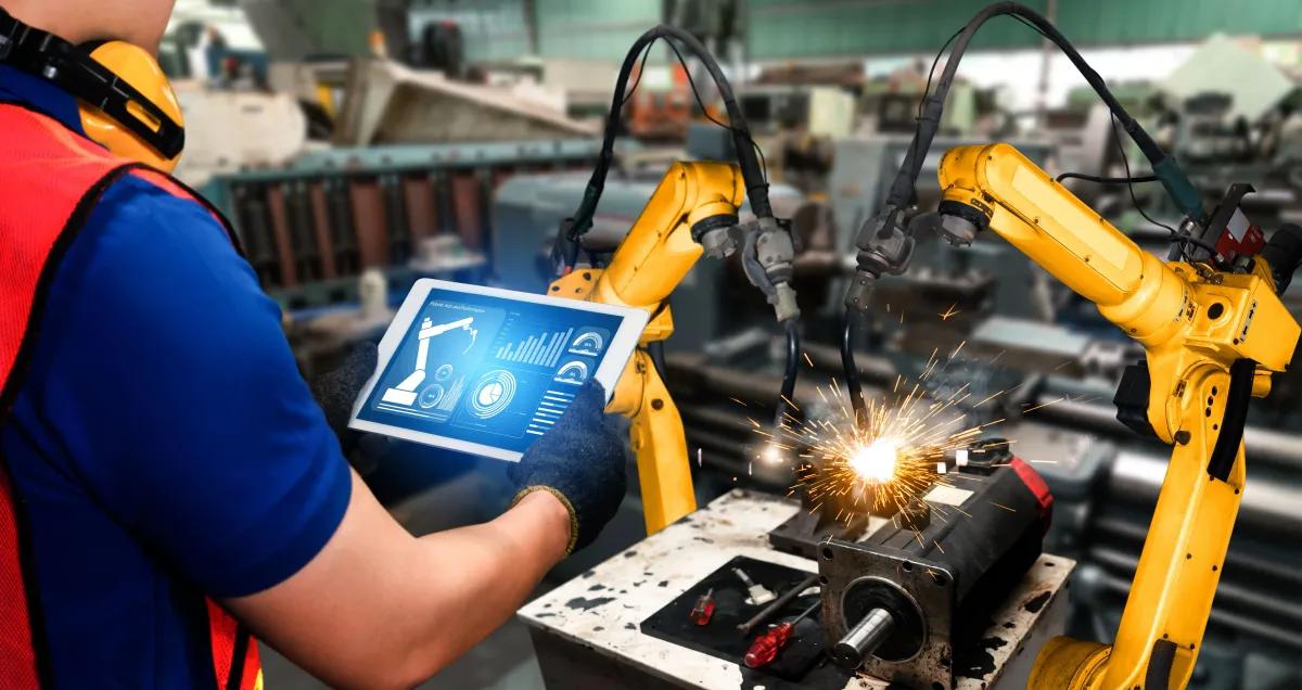 A man is using a tablet to control a robotic arm in a factory
