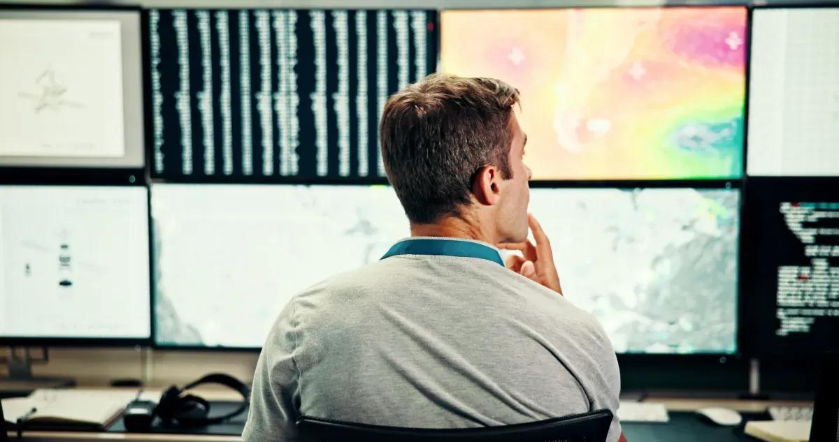 A man is sitting in front of a computer monitor in a control room