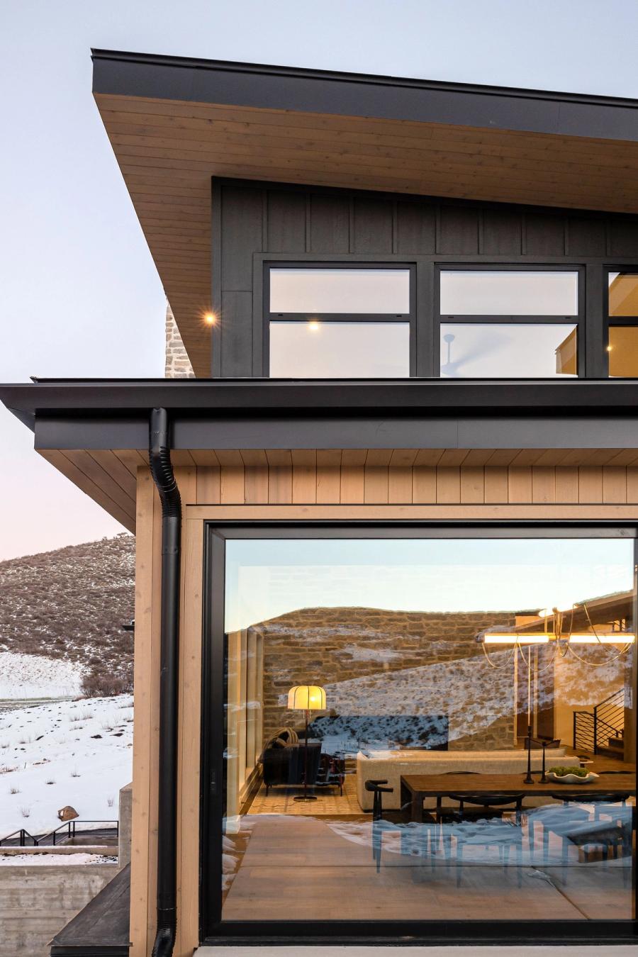 Dusk detail of Harris Way's wood and blackened-steel cladding with the Wasatch hillside reflected in the window wall