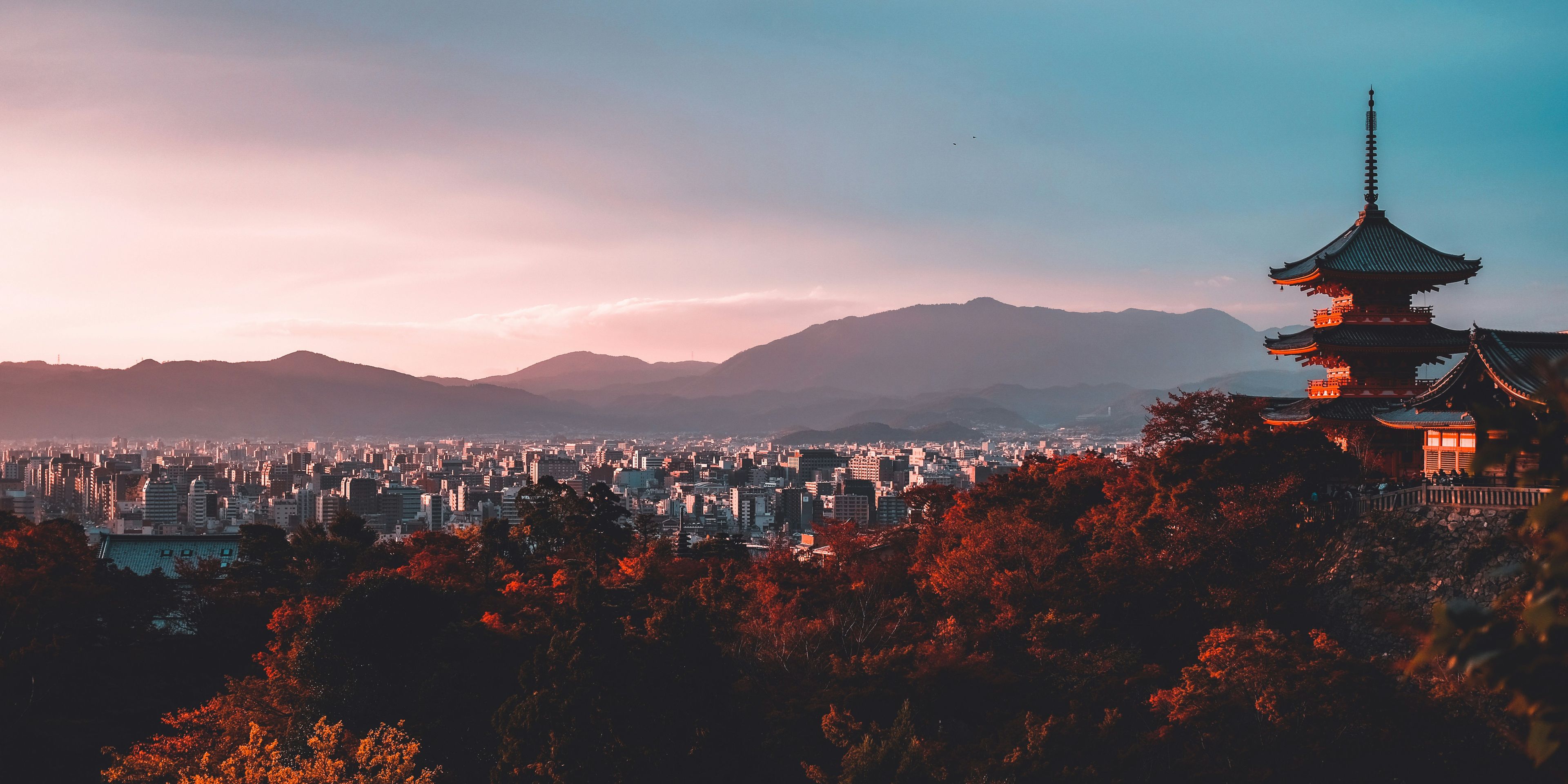 a city with a pagoda in the foreground and mountains in the background at sunset .