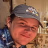 a man wearing a baseball cap and a plaid shirt is smiling for the camera .