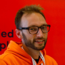 a man wearing glasses and an orange hoodie is smiling