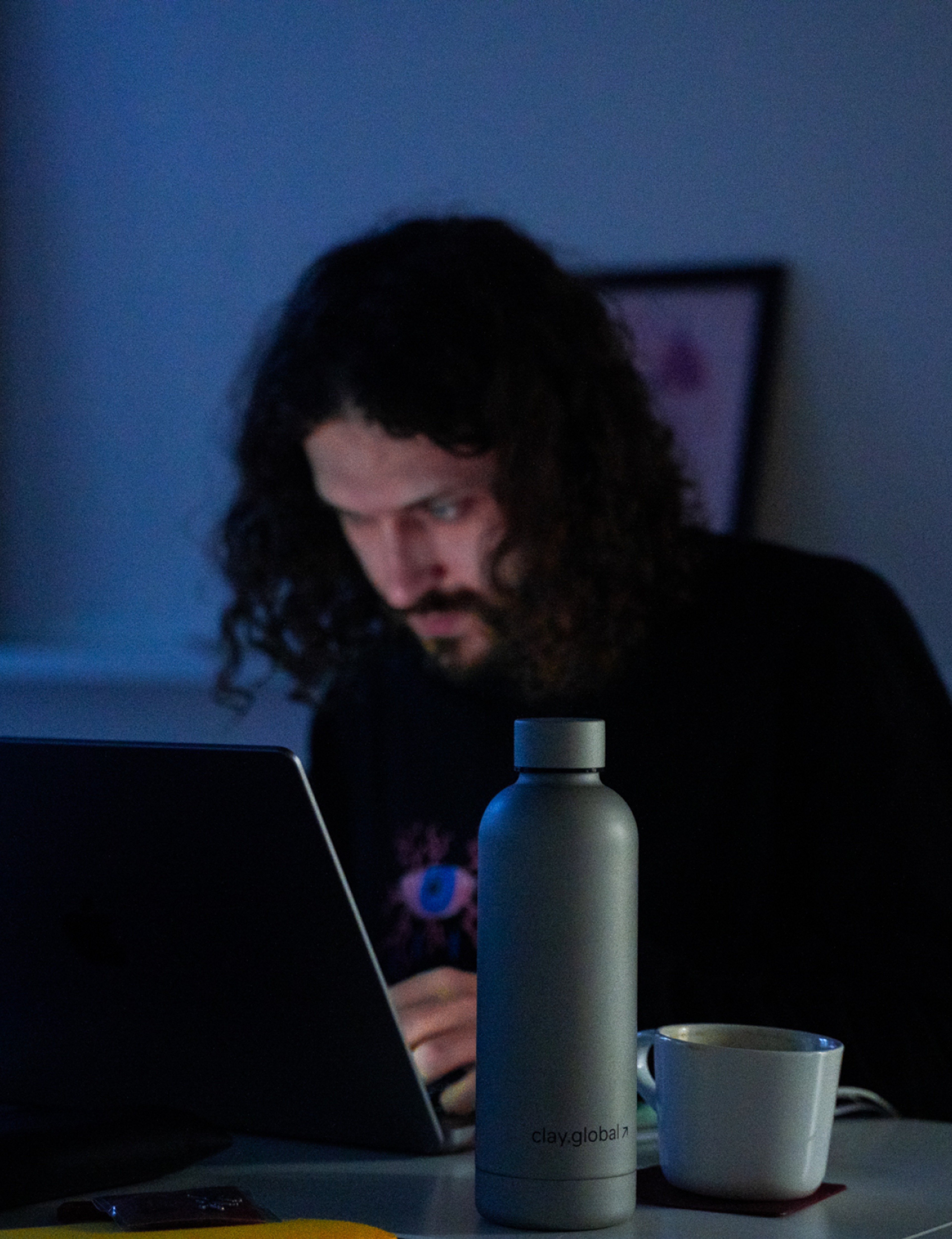 a Clay branded cup next to a person looking at a laptop 