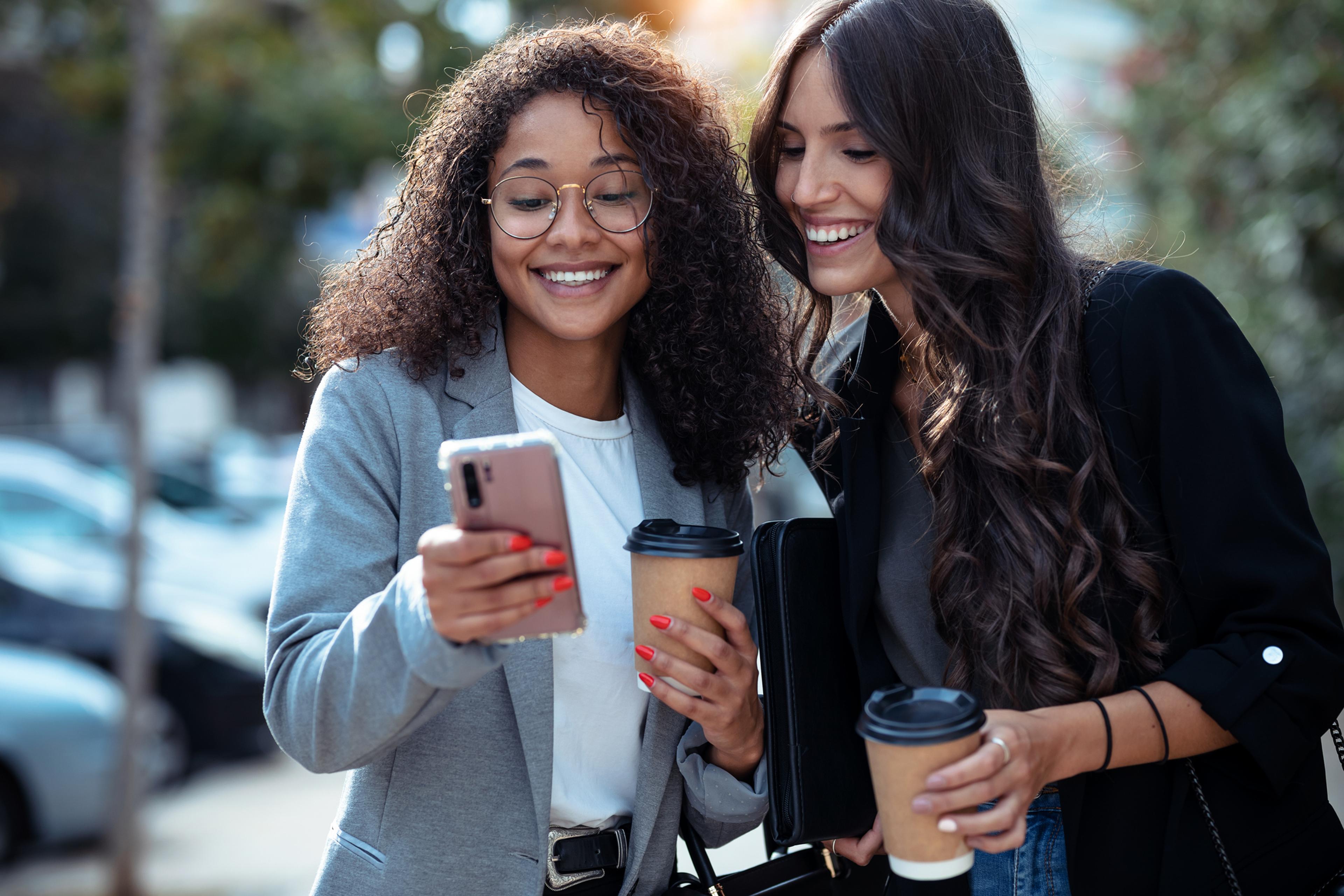 Two girls with coffee looking at a smartphone