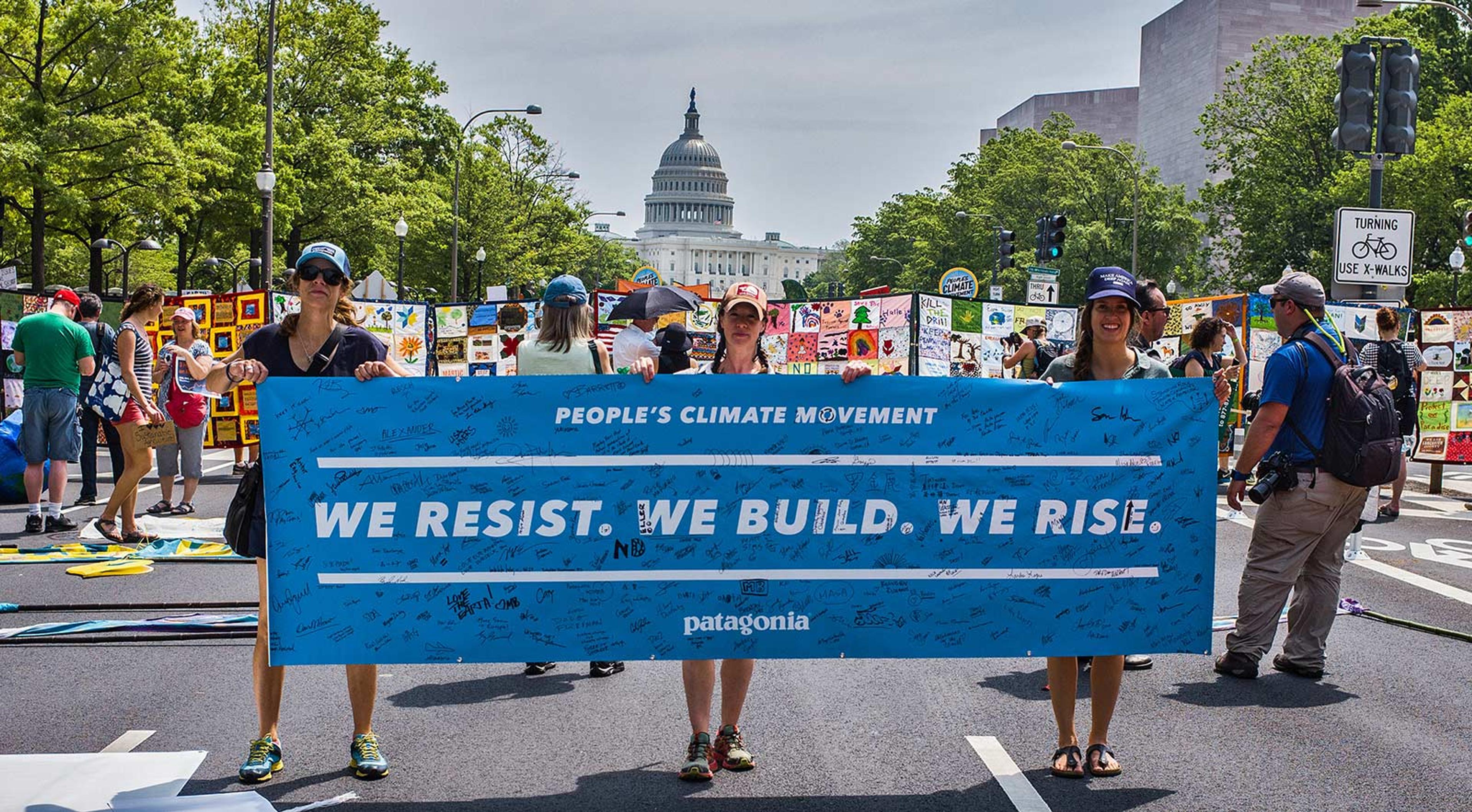 Three people holding a blue People's Climate Movement banner in the middle of the street