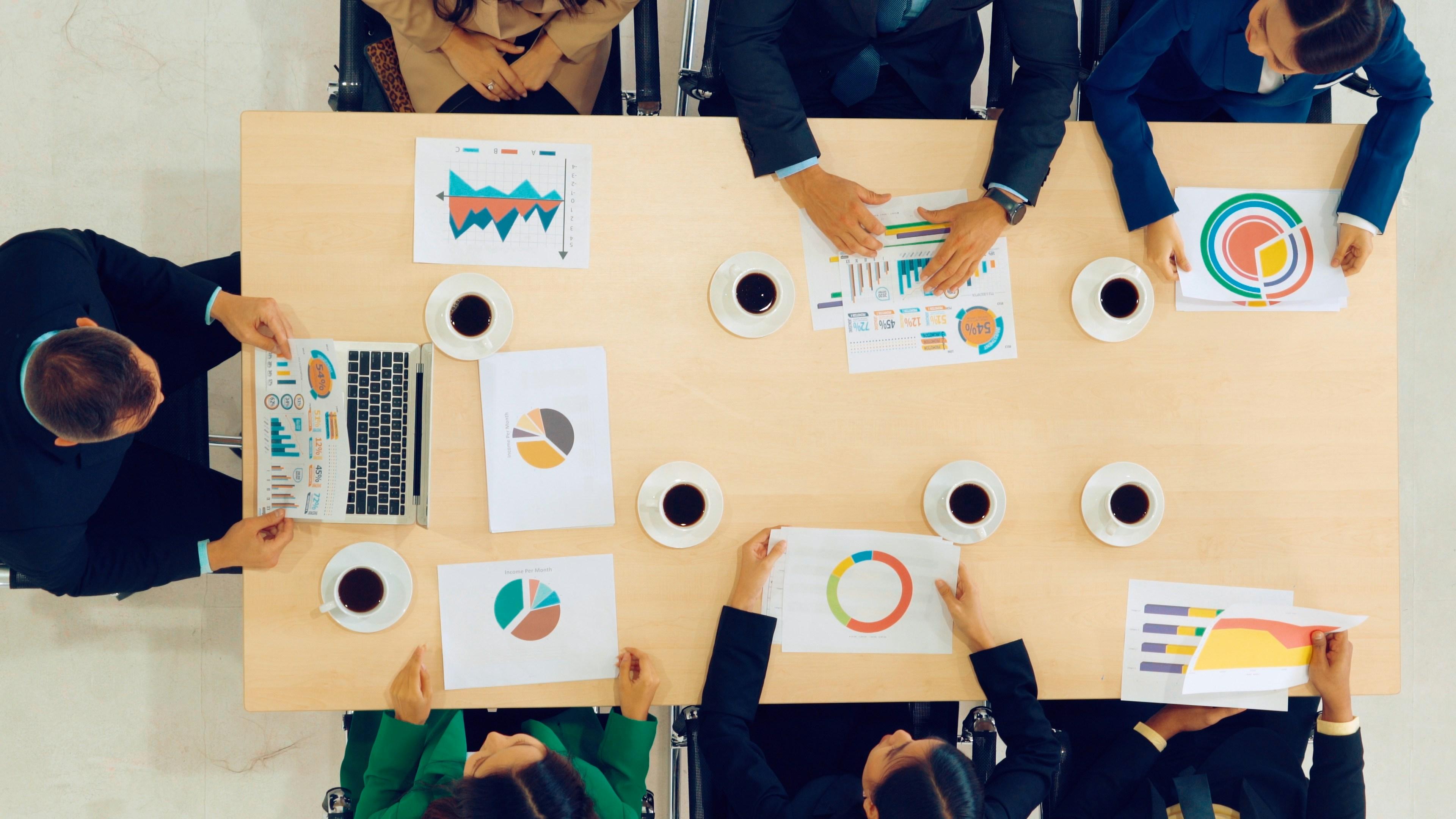 Seven people sitting at a table and discussing charts