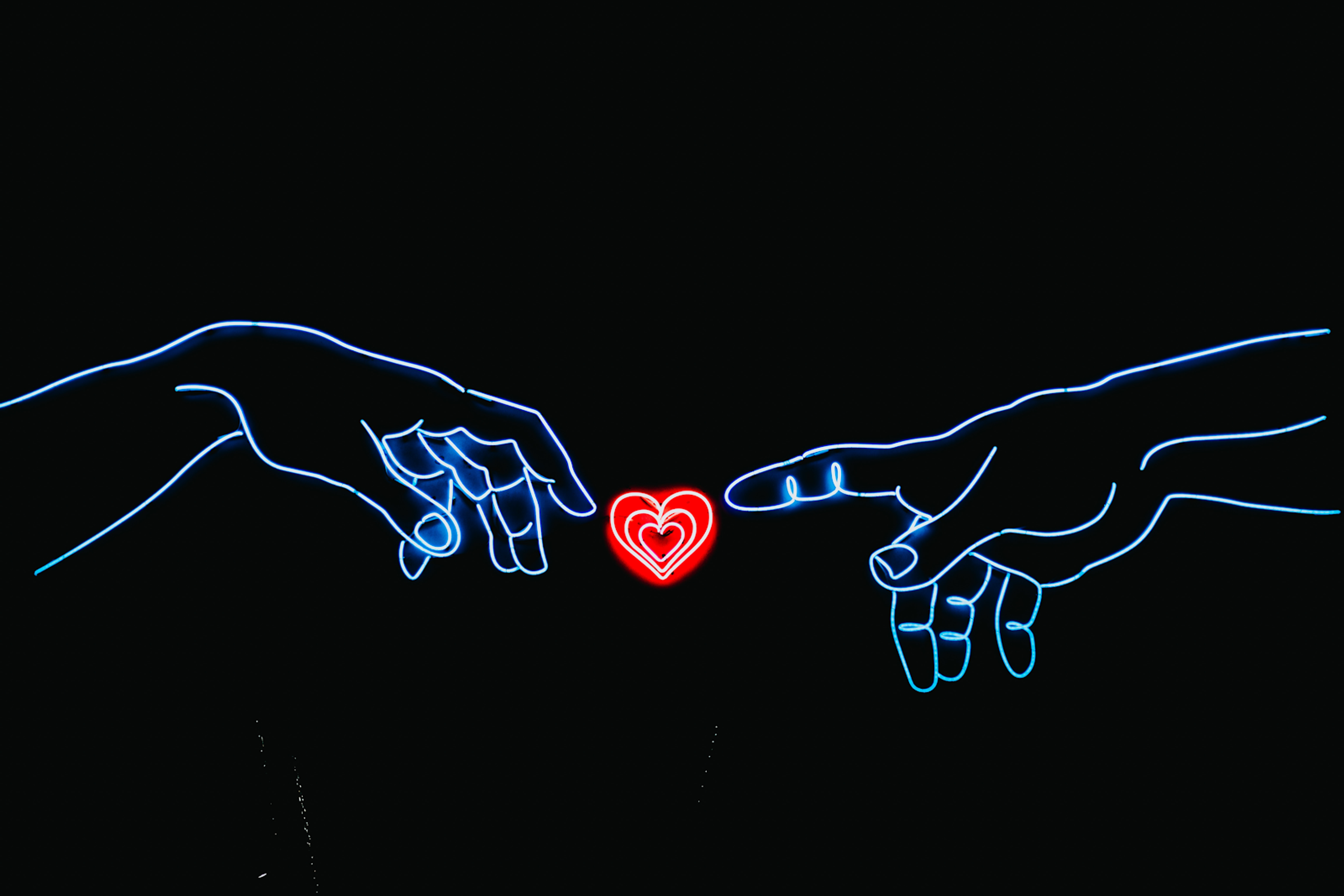 Two neon hands touching a heart between them