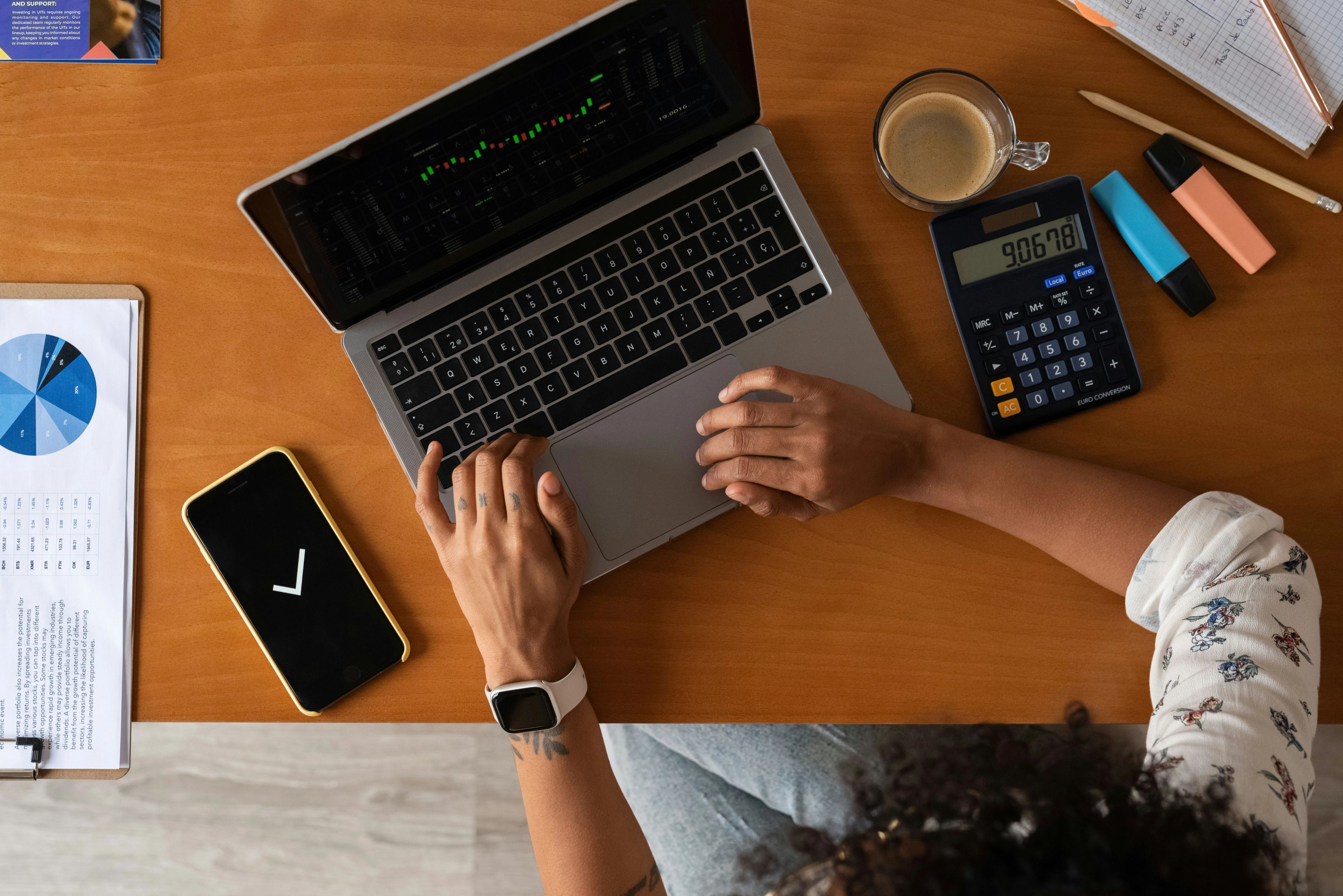 A person working on a laptop with a mobile phone and a calculator on a table