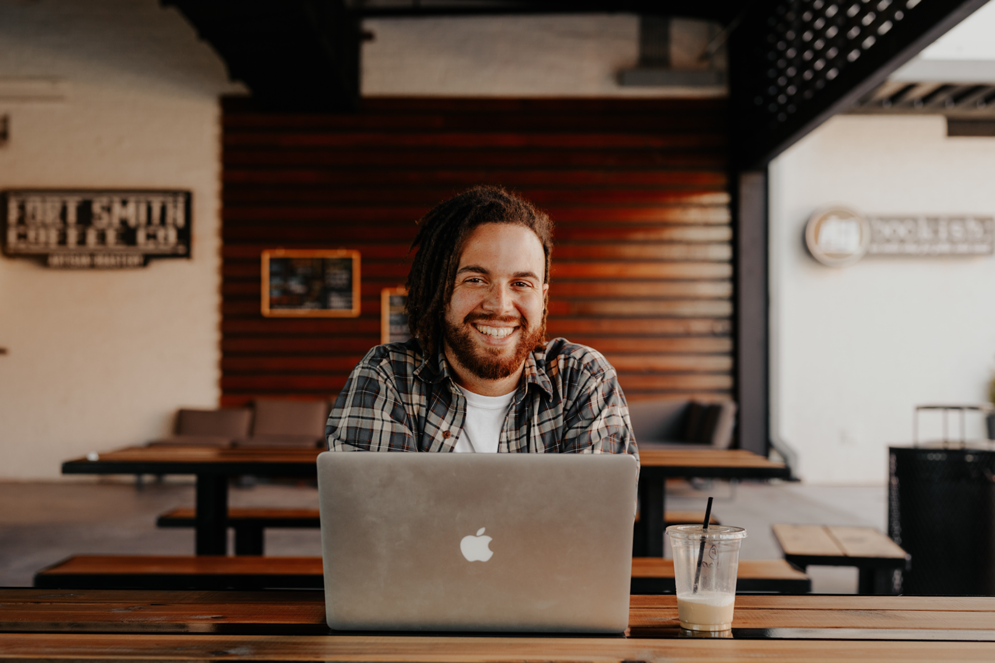A smiling man using a laptop and drinking coffee