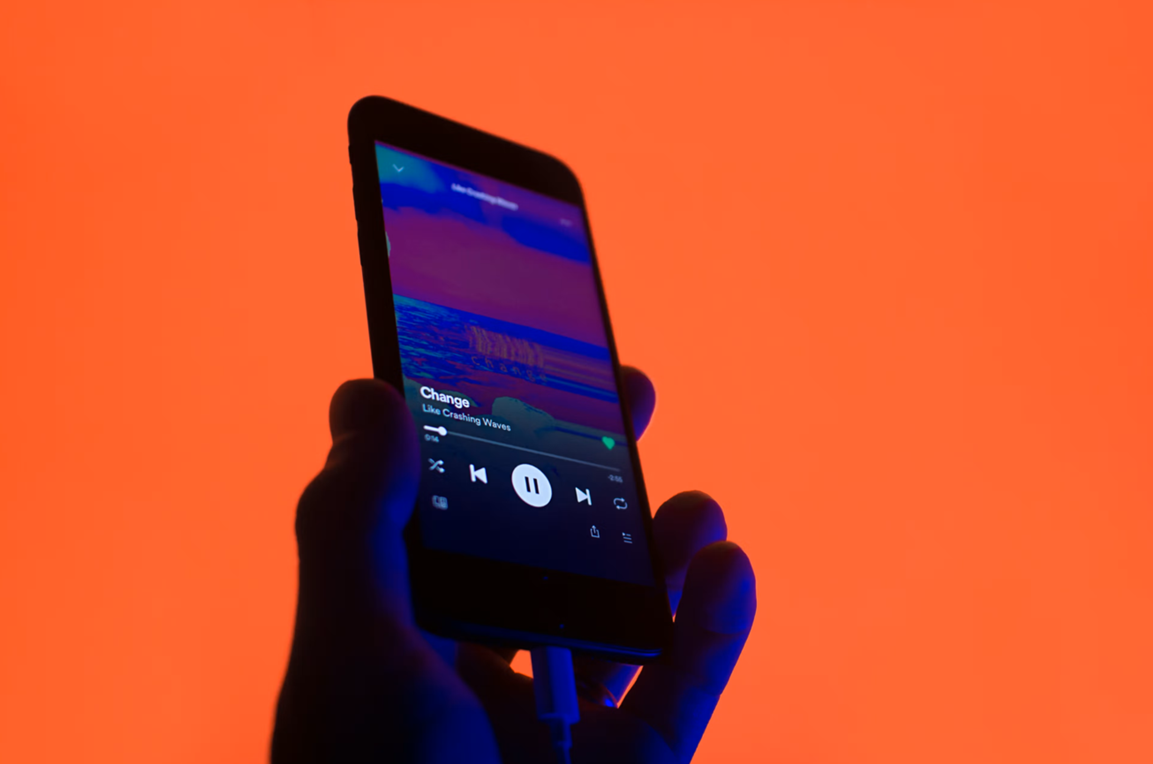 Hand holding a smartphone playing music with an orange background