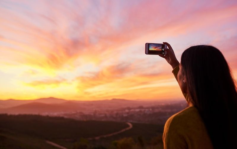 I want to remember this forever Rearview shot of a woman taking a photo of a sunset with her smartphone