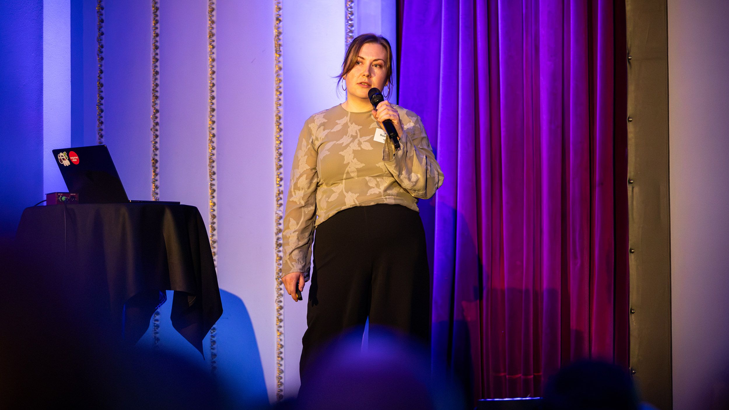 Jenni Suominen lavalla puhumassa mikrofoni kädessä Shine Sessions -tapahtumassa.