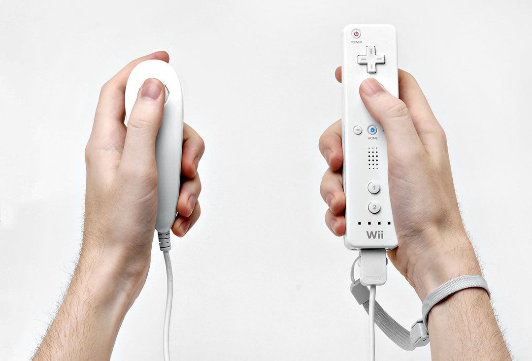 Käsissä valkoiset Nintendo Wii -pelikonsolin ohjaimet