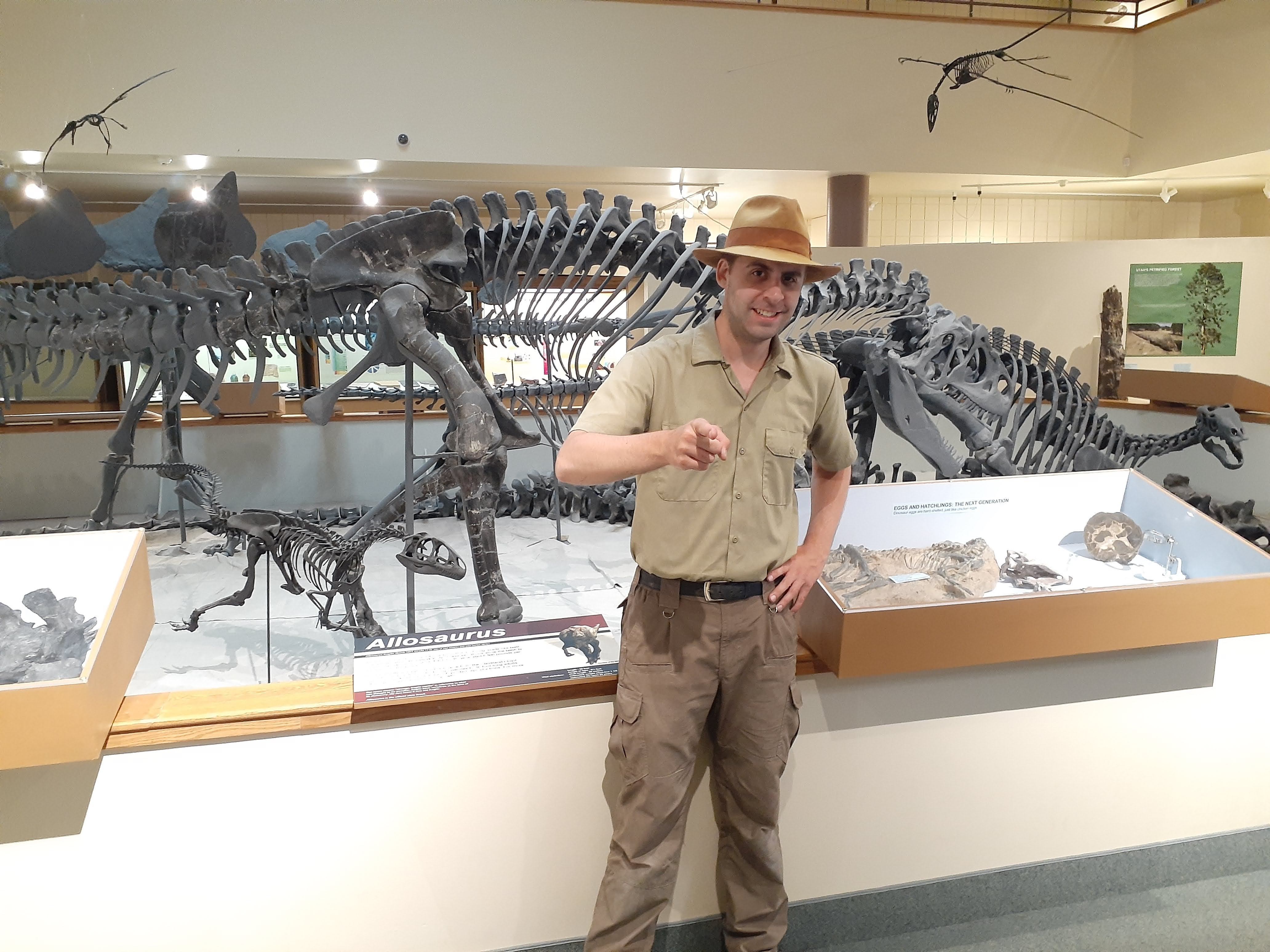 Man pointing at camera with dinosaur skeleton behind him