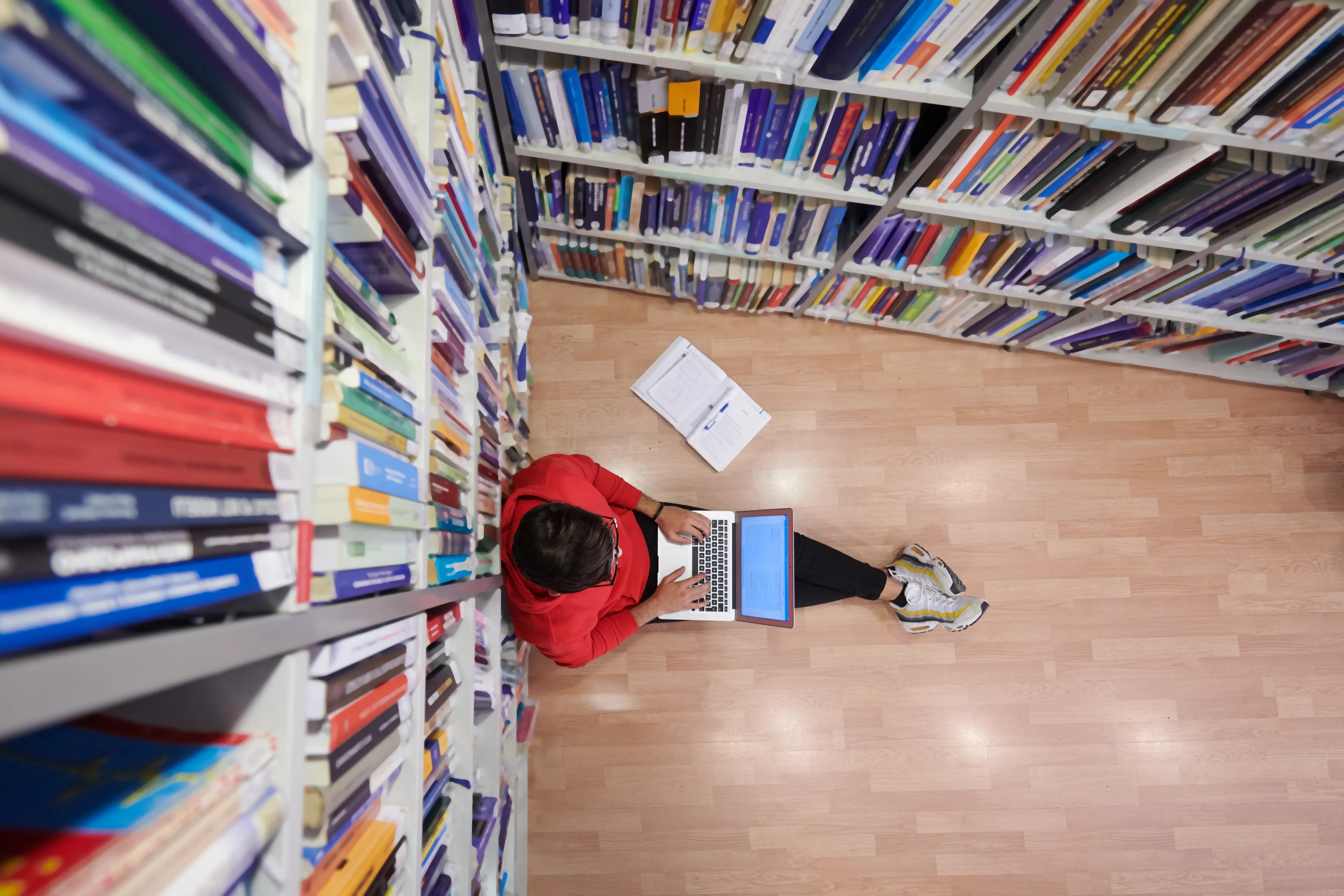 Student sitting down on a computer surrounded by books