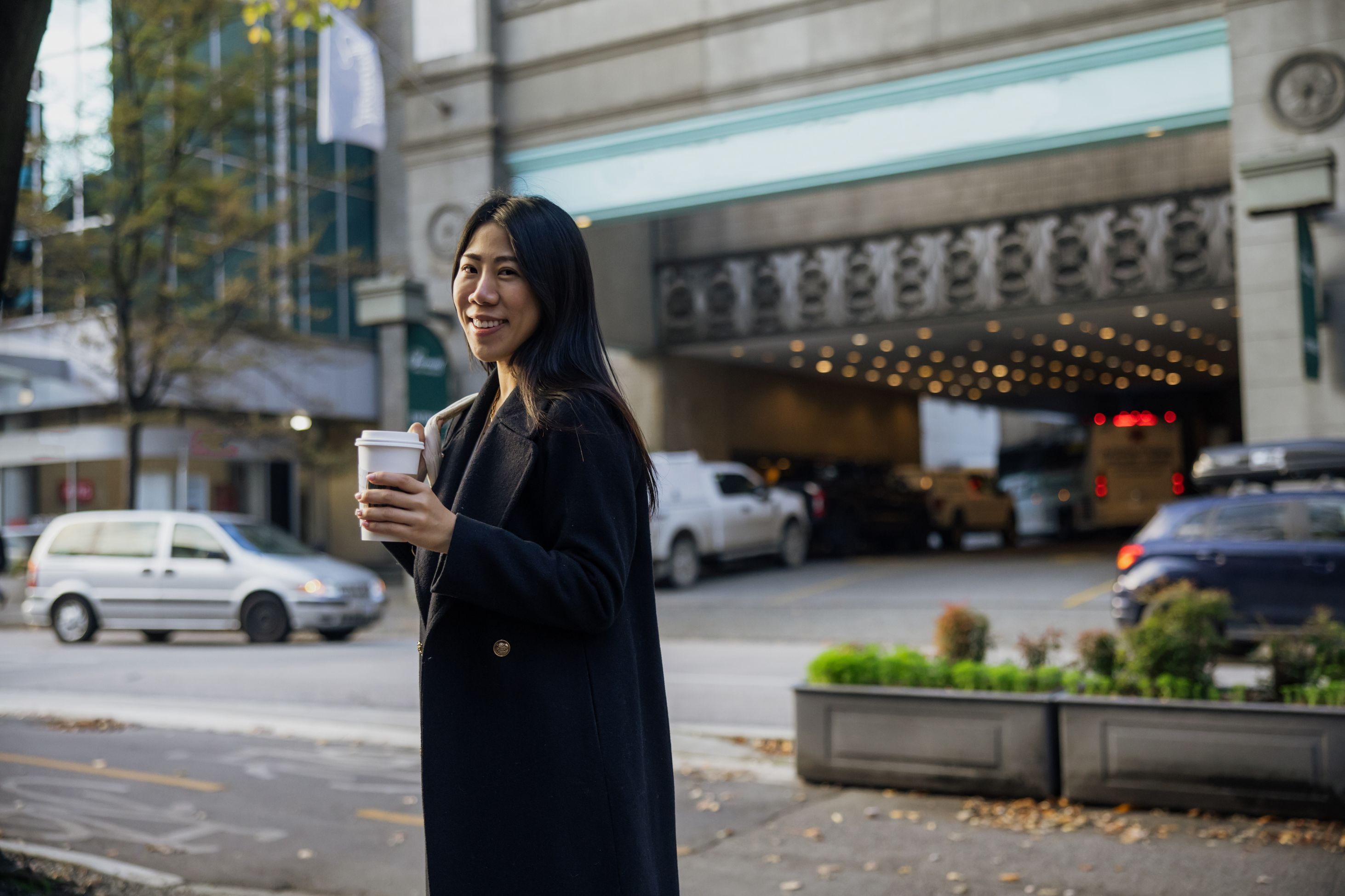 A smiling young businesswoman holding a cup of coffee on a city street