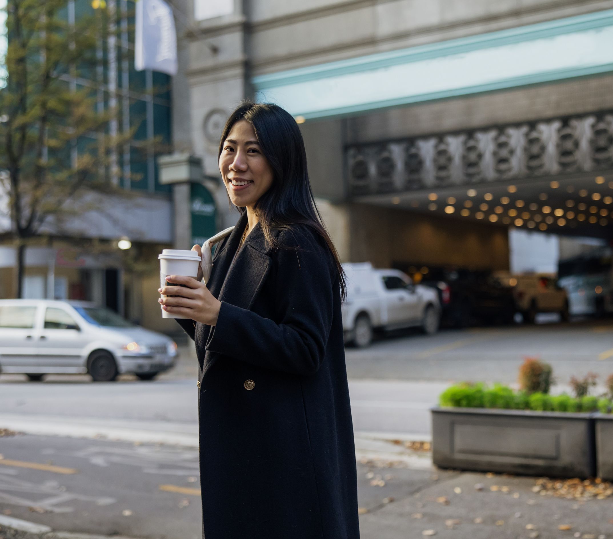 A smiling young businesswoman holding a cup of coffee on a city street