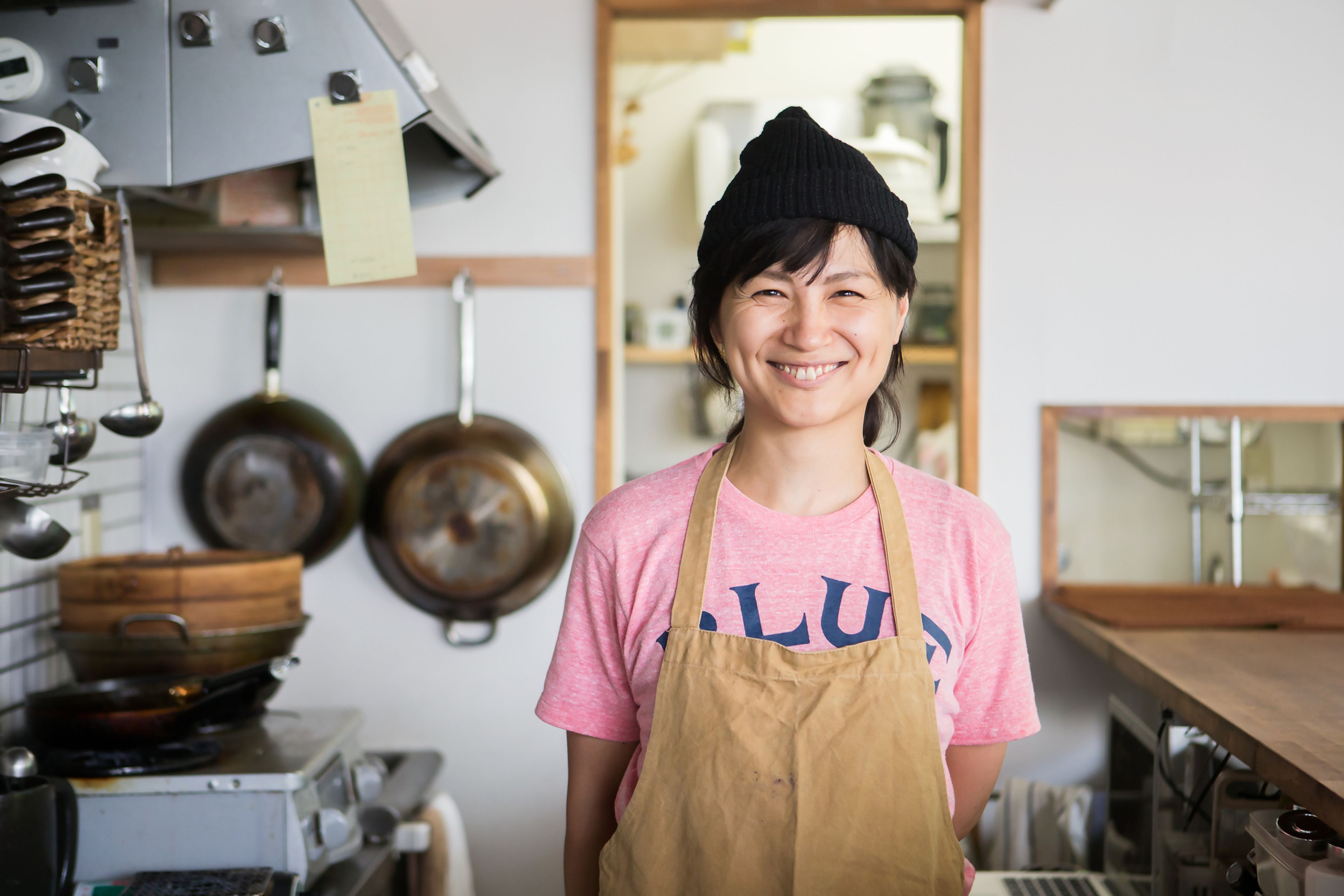 A smiling cafe owner wearing an apron stood in a kitchen