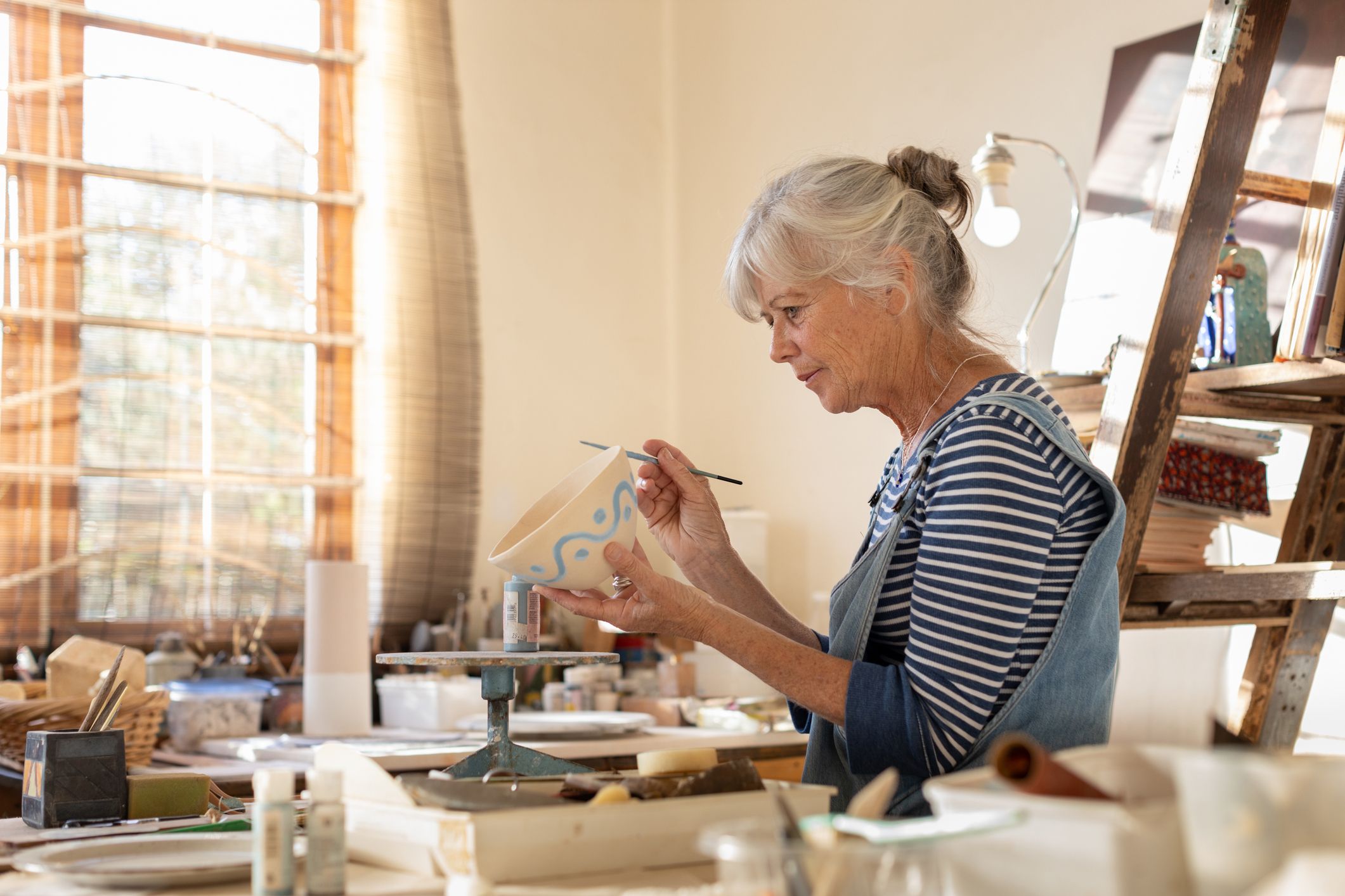 A middle aged woman in a pottery workshop, painting a hand-made bowl