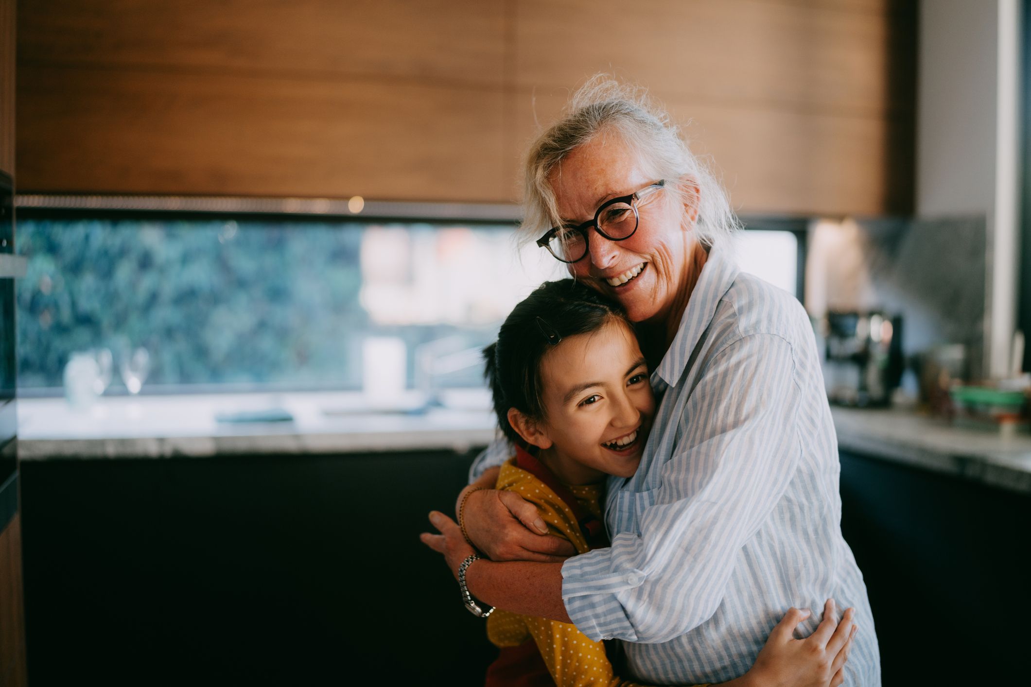 A grandmother and held grandchild smiling and hugging in the family kitchen