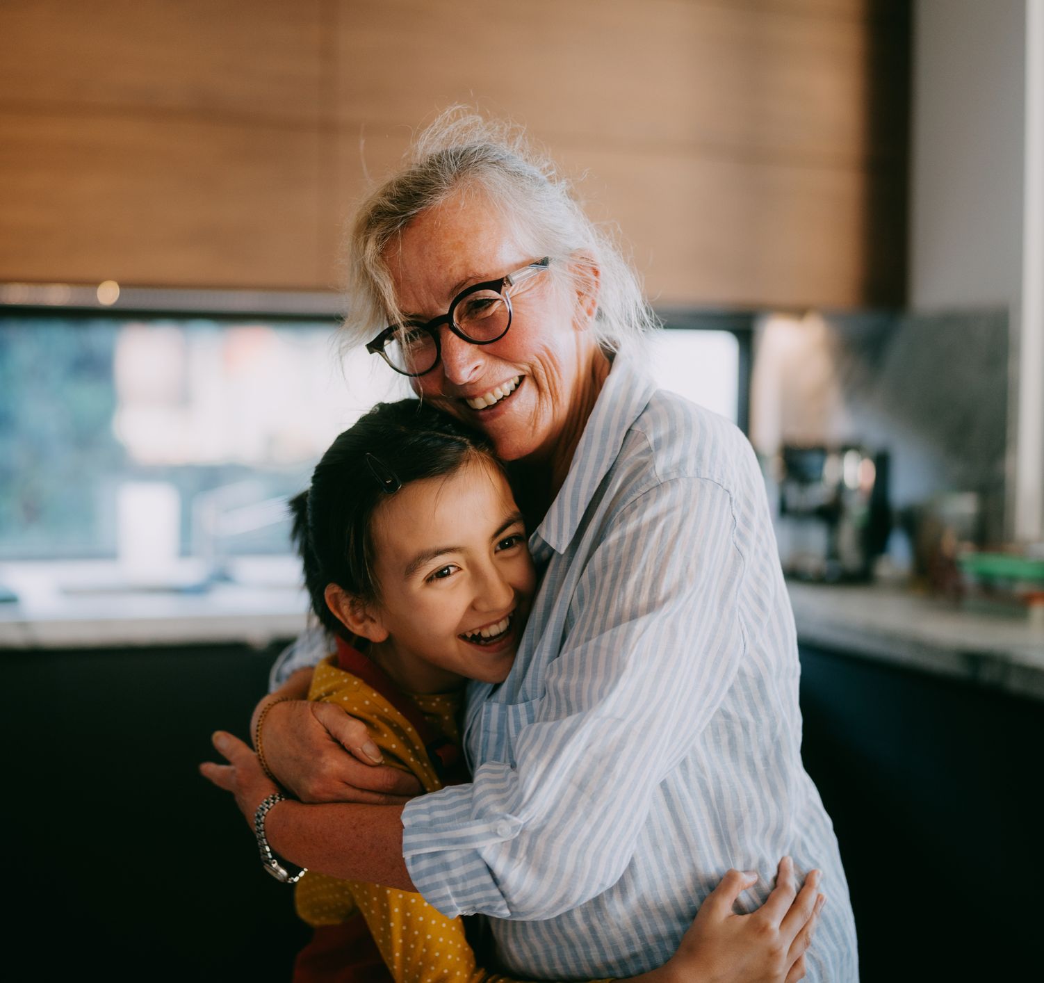 A grandmother and held grandchild smiling and hugging in the family kitchen