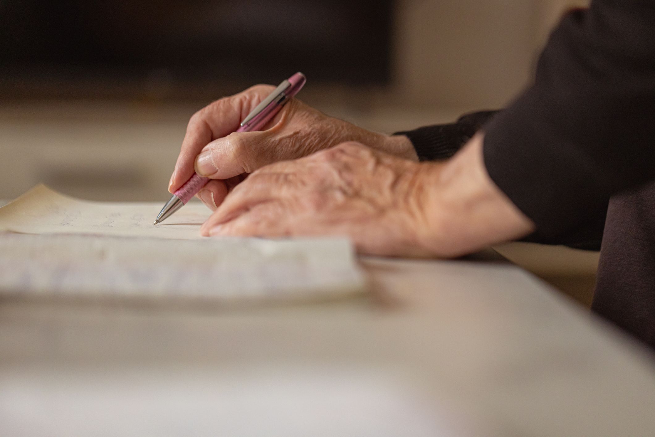 Close up of a pair of hands, the right holding a pen, writing on a document