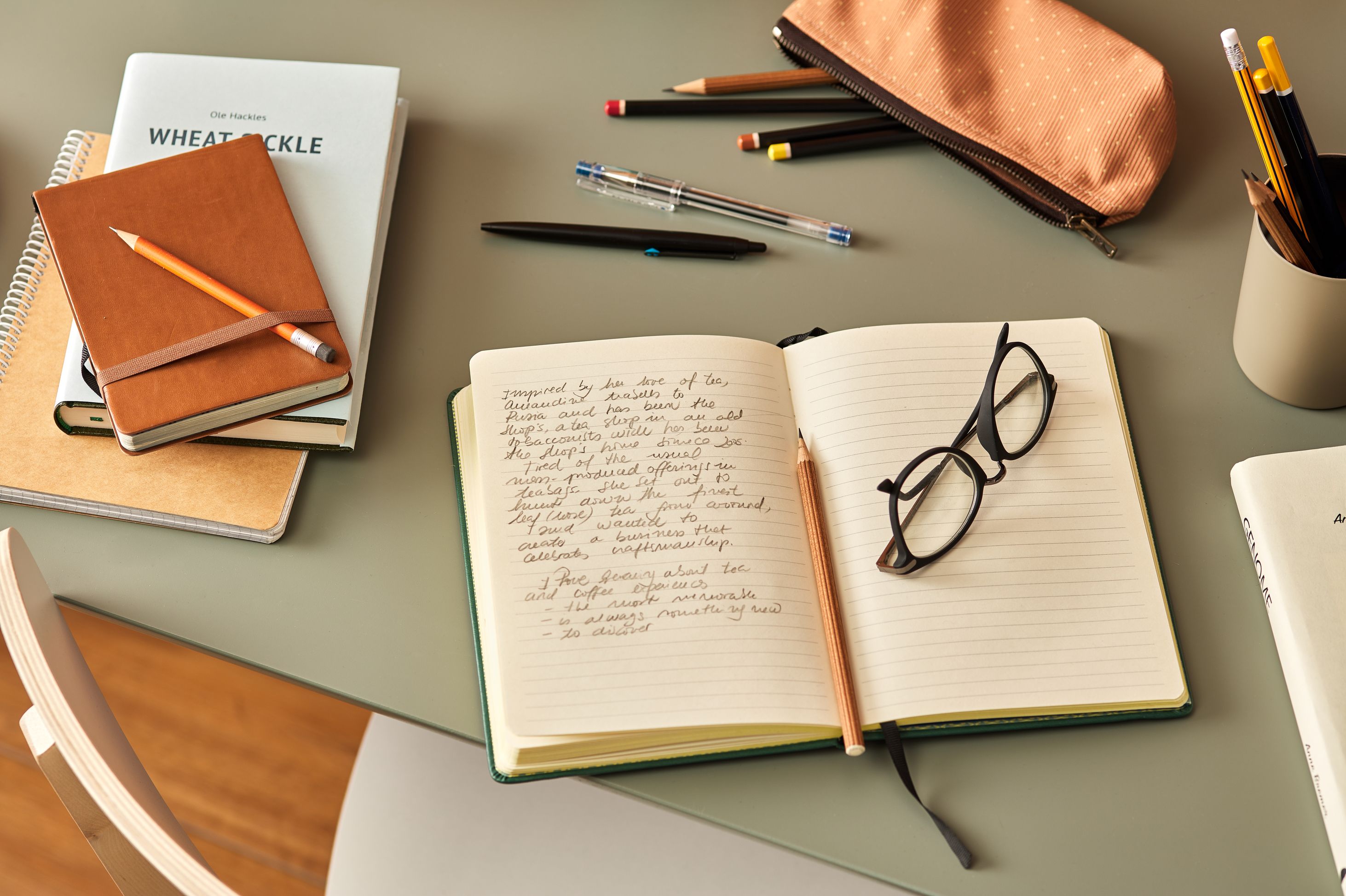 An open notebook with a pencil resting in the fold next to a pair of glasses