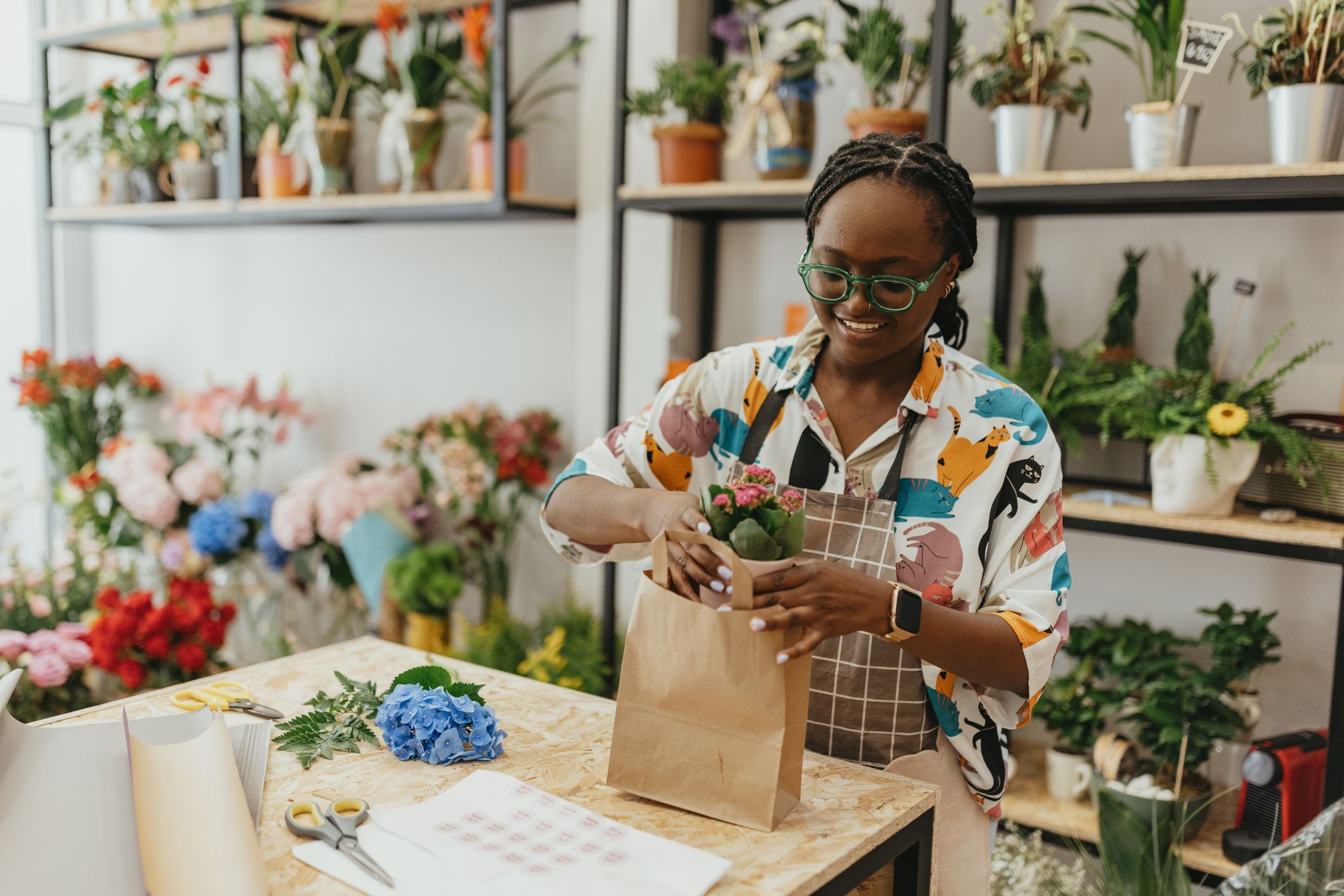 A smiling plant store owner stood behind a counter, bagging a small potted plant