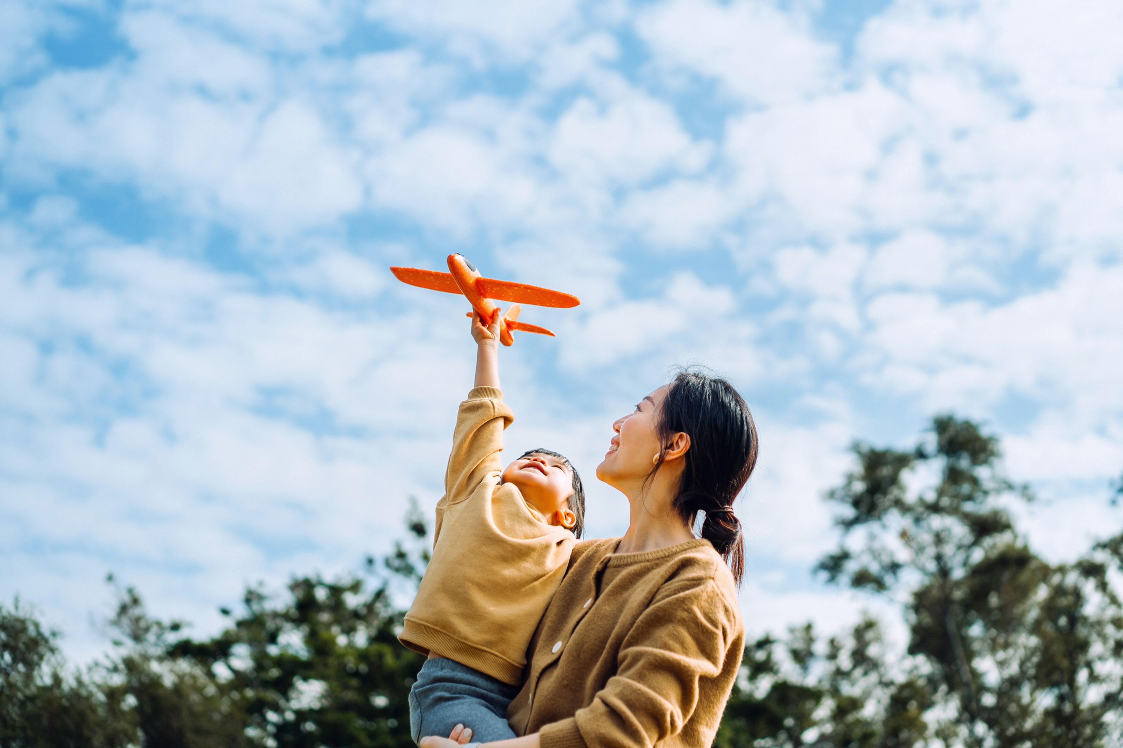 A child's hand holding a toy airplane up to the sky